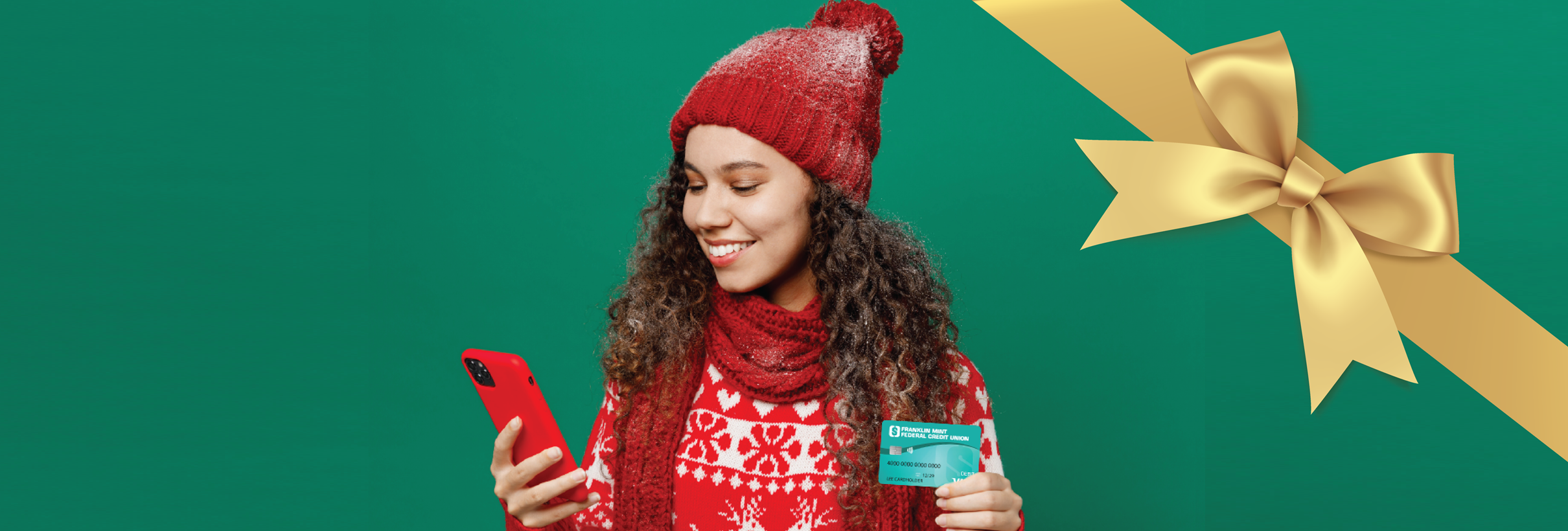 Woman in winter holiday clothing holding a phone and FMFCU Debit Card, to promote using Digital Wallets during the holiday season.